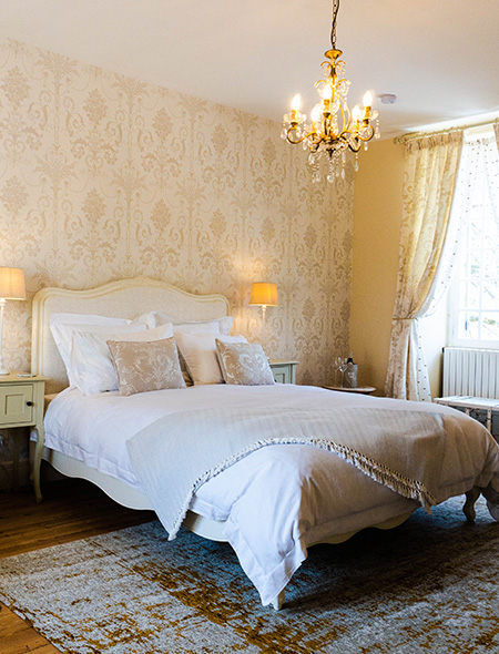Logis de Tirac bedroom - Kingsize bed, sunny day, cream interior, chandelier, and large French windows.