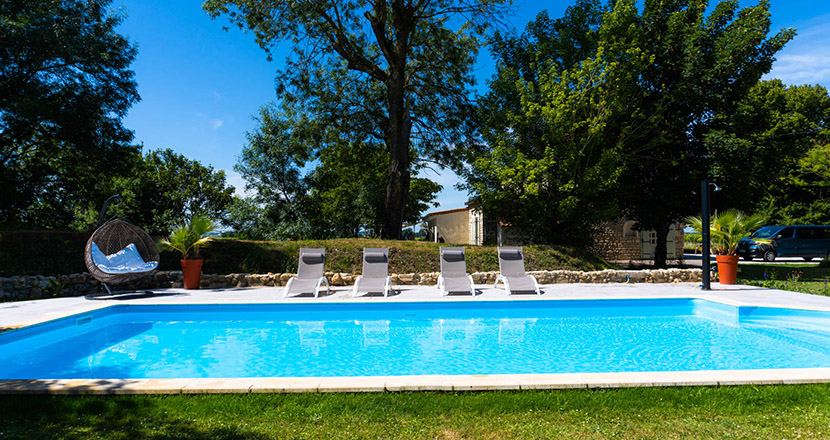 Logis-de-Tirac-pool in the sun with sunbeds on the grass, blue swimming pool, and the large French house in the background on a summer day